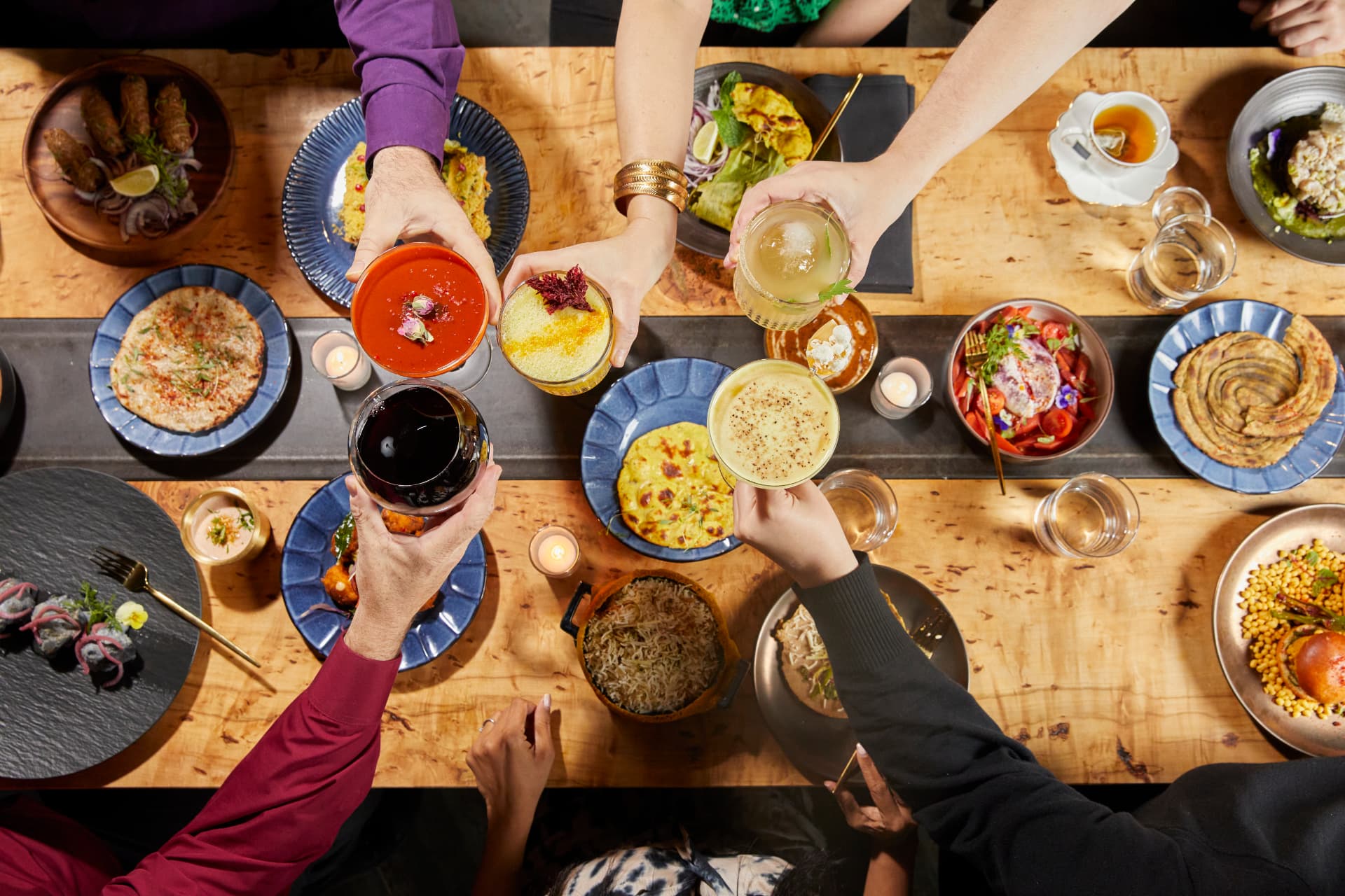 Hands raising cocktails over a table of Kricket Club dishes